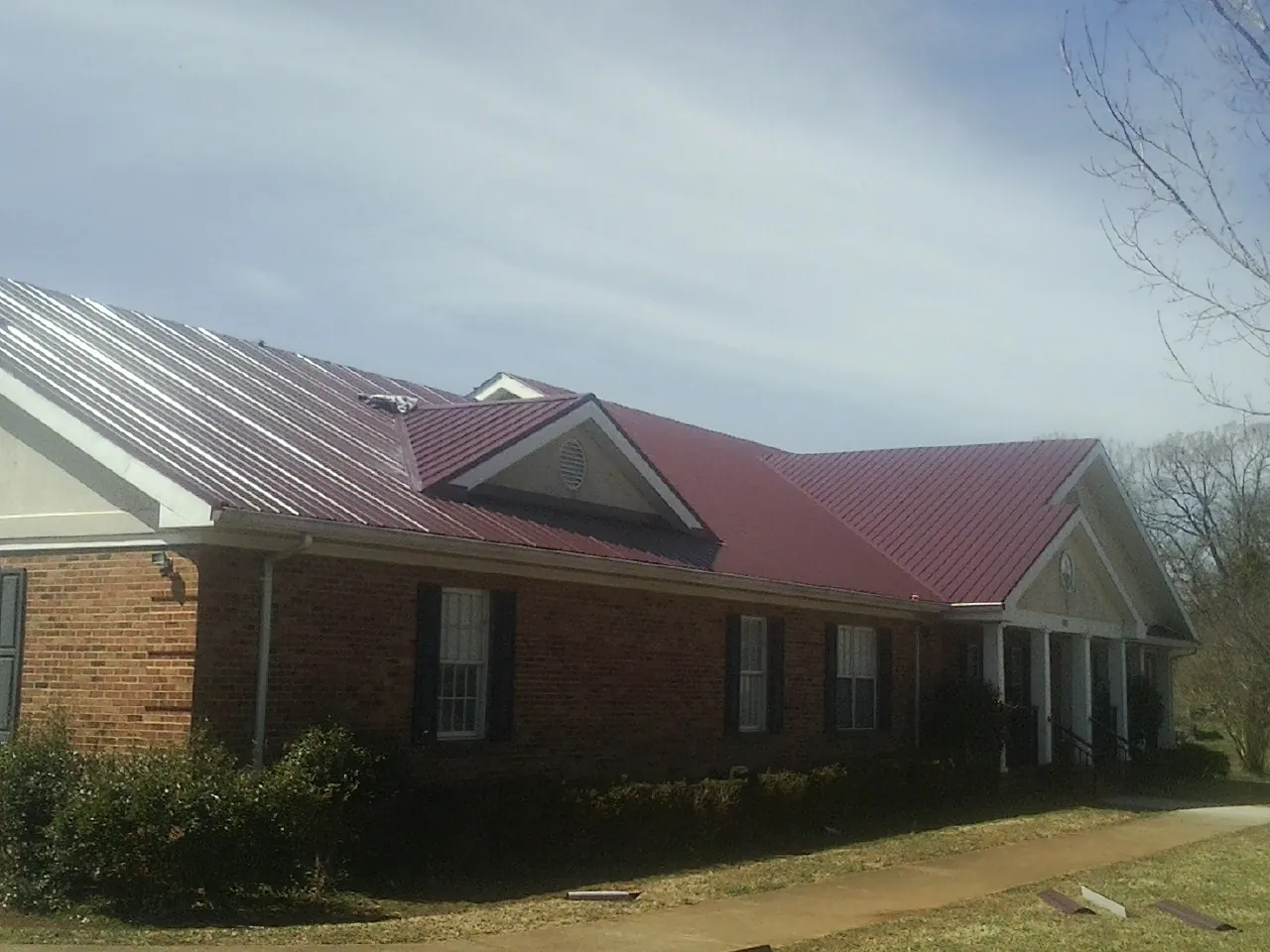 Red metal roof with gabled entries on a long brick building, from a Hail Damage Roof Repair job in Fowler