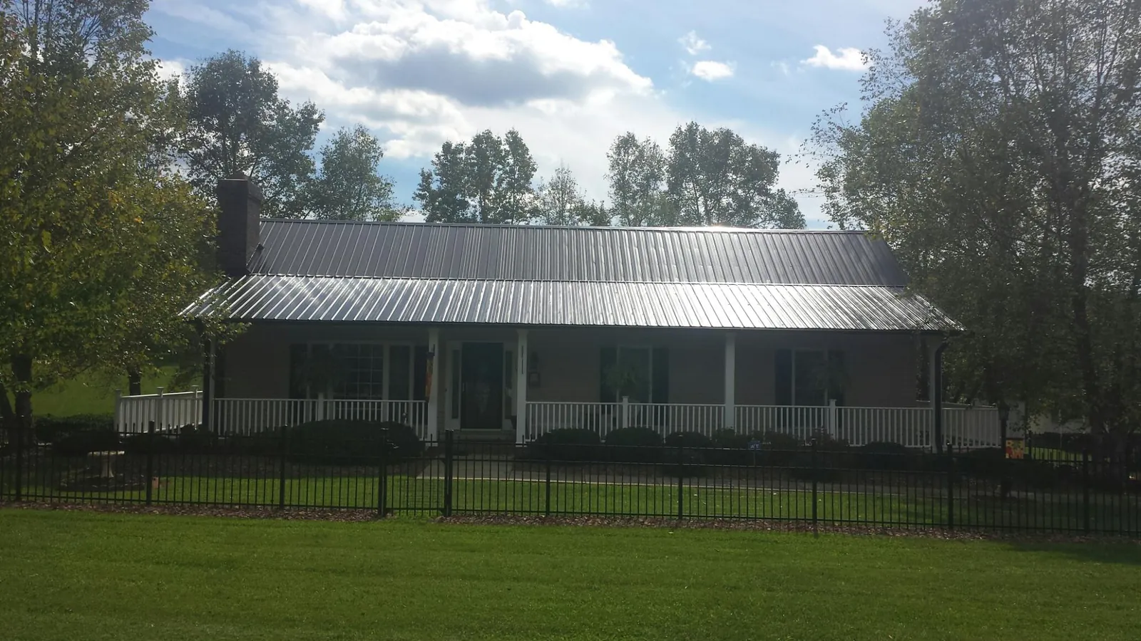 Gray metal roof on a brick ranch with a full width front porch — Gutter Guard Installation work by our crew in Fowler