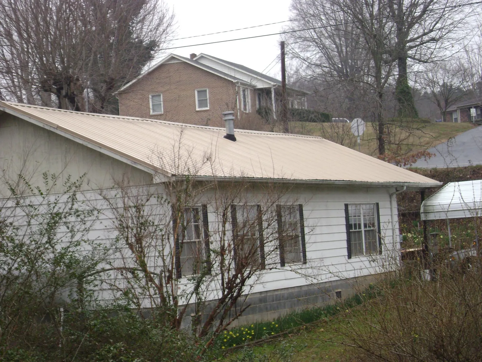 Tan metal roof on a white sided house set into a hillside — Commercial Roofing by Roofing Brothers in Fowler